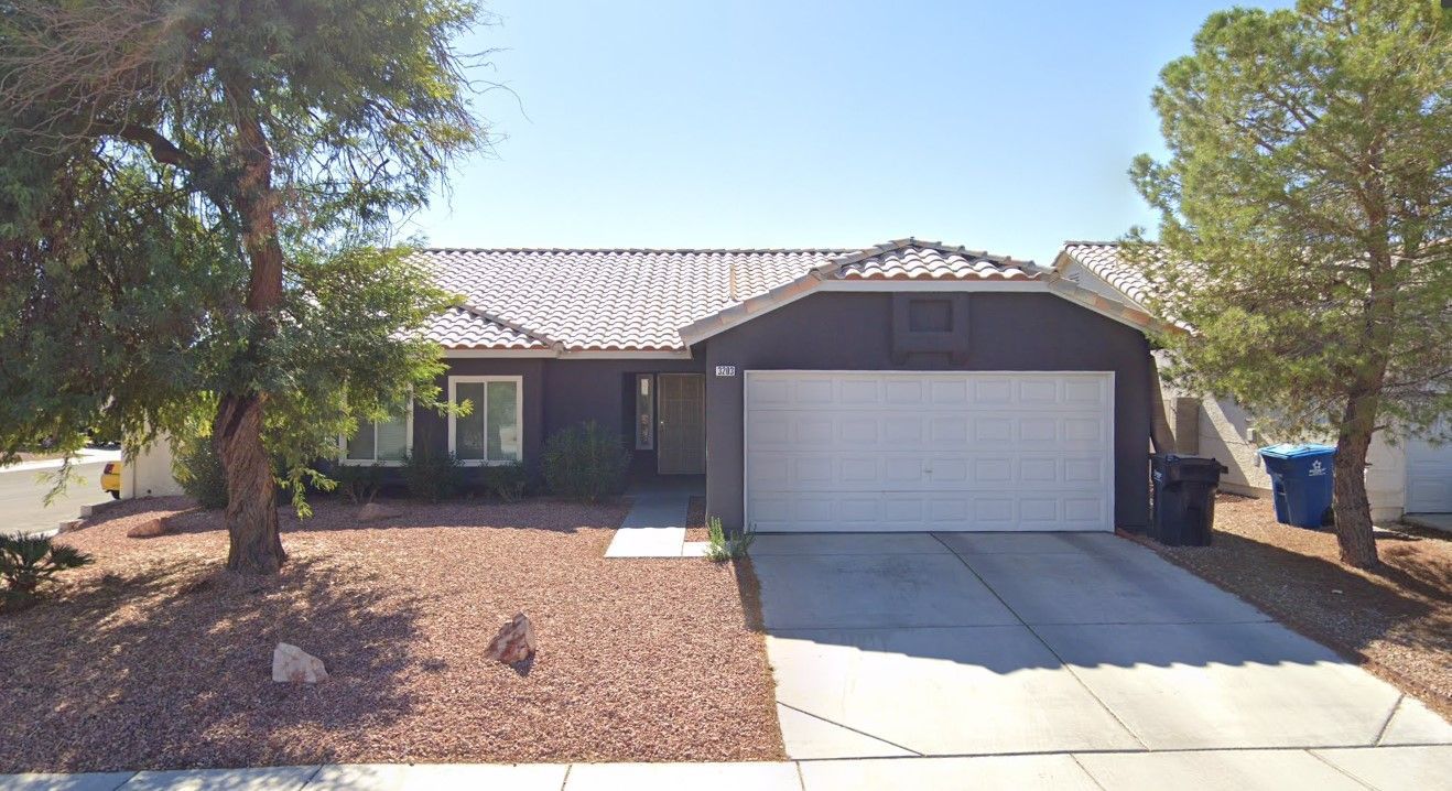 Brown ranch-style house with a white garage door, brown gravel yard, and a clear blue sky.