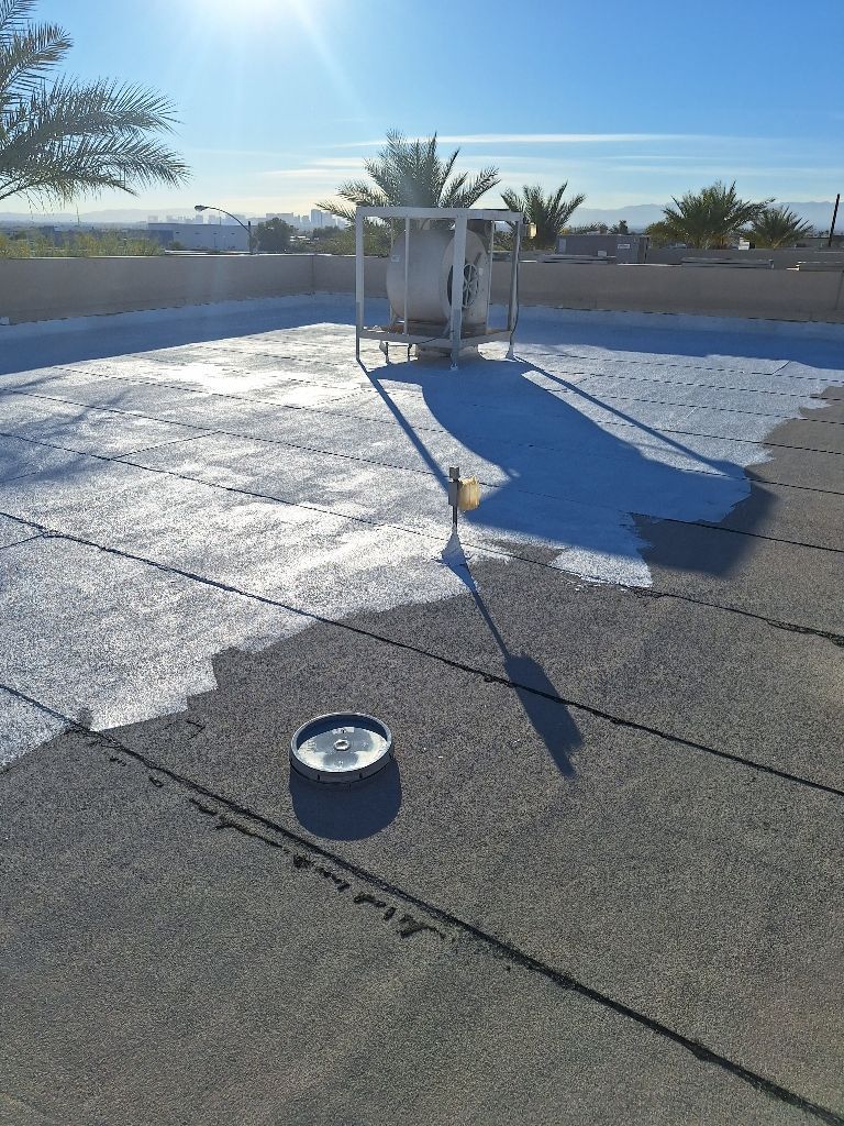 Flat roof with a white structure, a shadow, and a small circular device in the sunlight.
