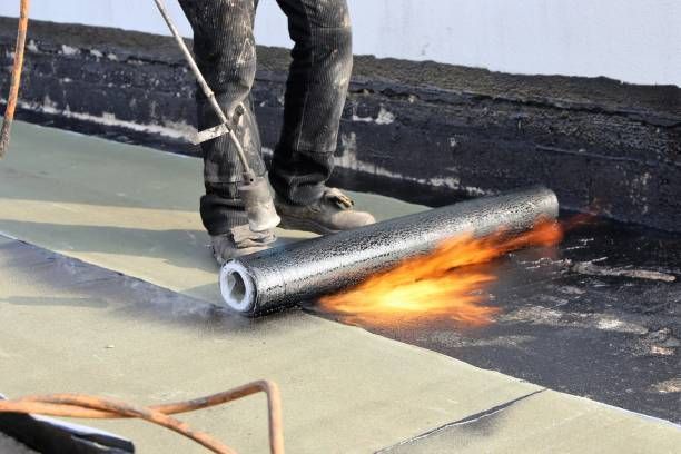 Roofer using a torch to apply a black, rolled roofing material to a flat roof.