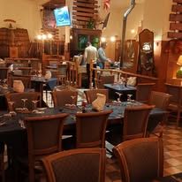 Interno del ristorante con tavoli, sedie e decorazioni. Luci soffuse, mobili in legno e un bar.