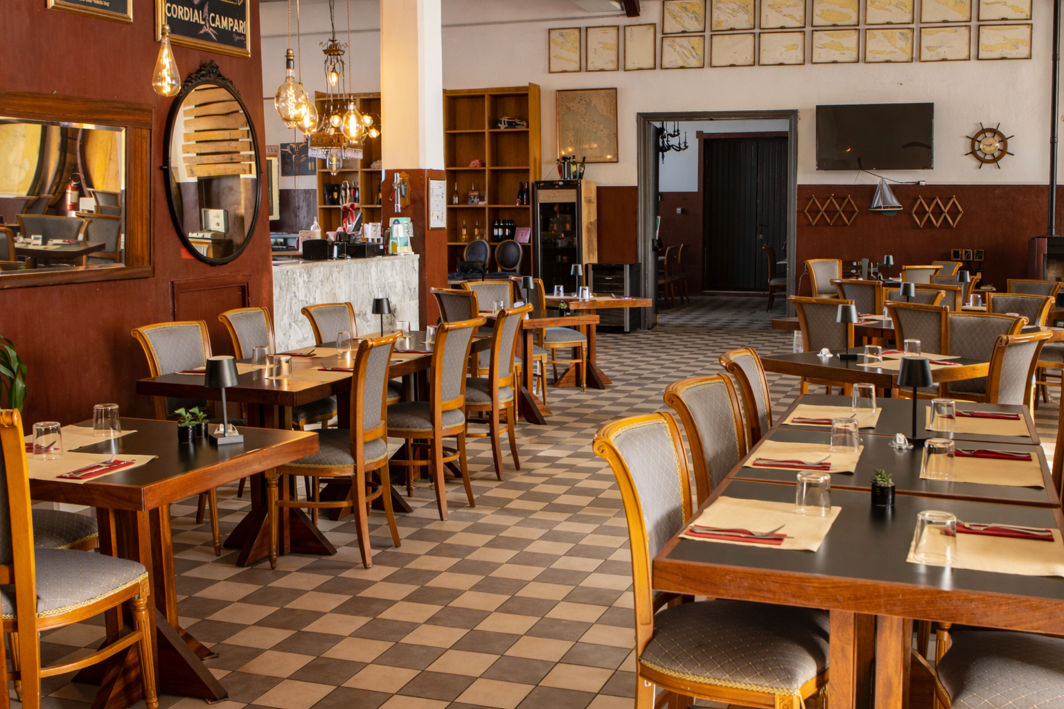 Interno del ristorante con tavoli, sedie e decorazioni. Luci soffuse, mobili in legno e un bar.