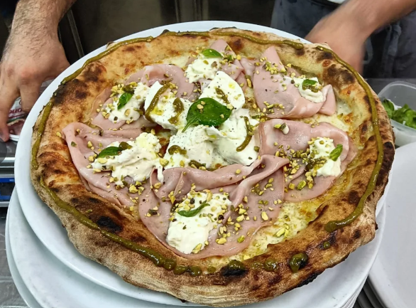 Pizza condita con mortadella, mozzarella, pistacchi e basilico.