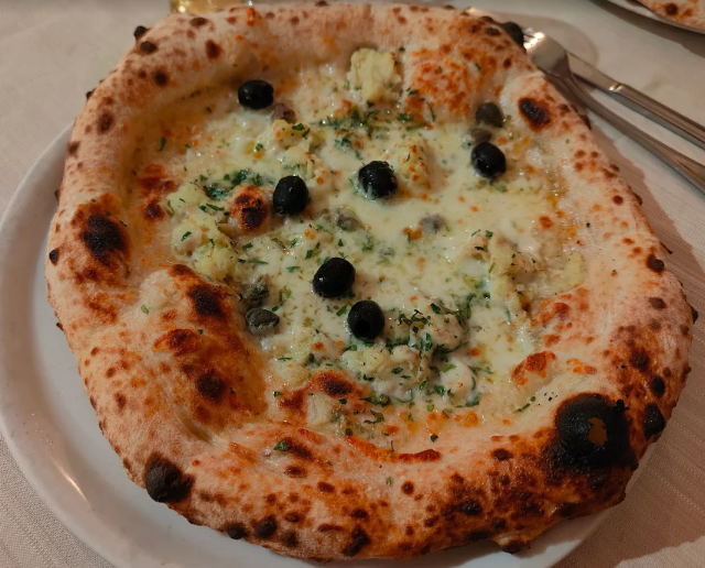 Pizza con besciamella, olive ed erbe aromatiche su un piatto bianco.