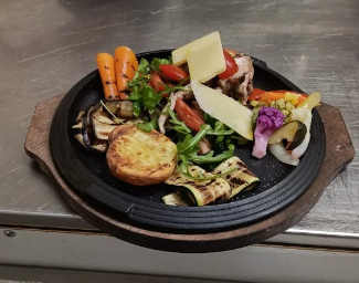 Verdure grigliate e formaggio su un piatto nero con manici in legno.