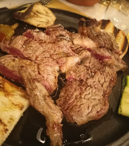 Bistecca alla griglia tagliata con verdure grigliate su un piatto nero.