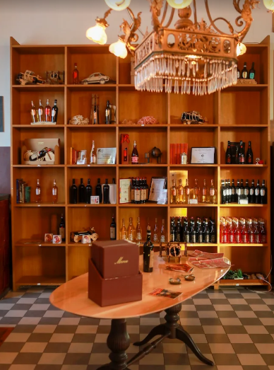 Scaffali di legno pieni di bottiglie e barattoli, con un tavolo ovale in primo piano.