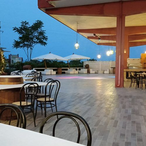 Patio esterno del ristorante con tavoli, sedie, ombrelloni e luci a filo, al tramonto.