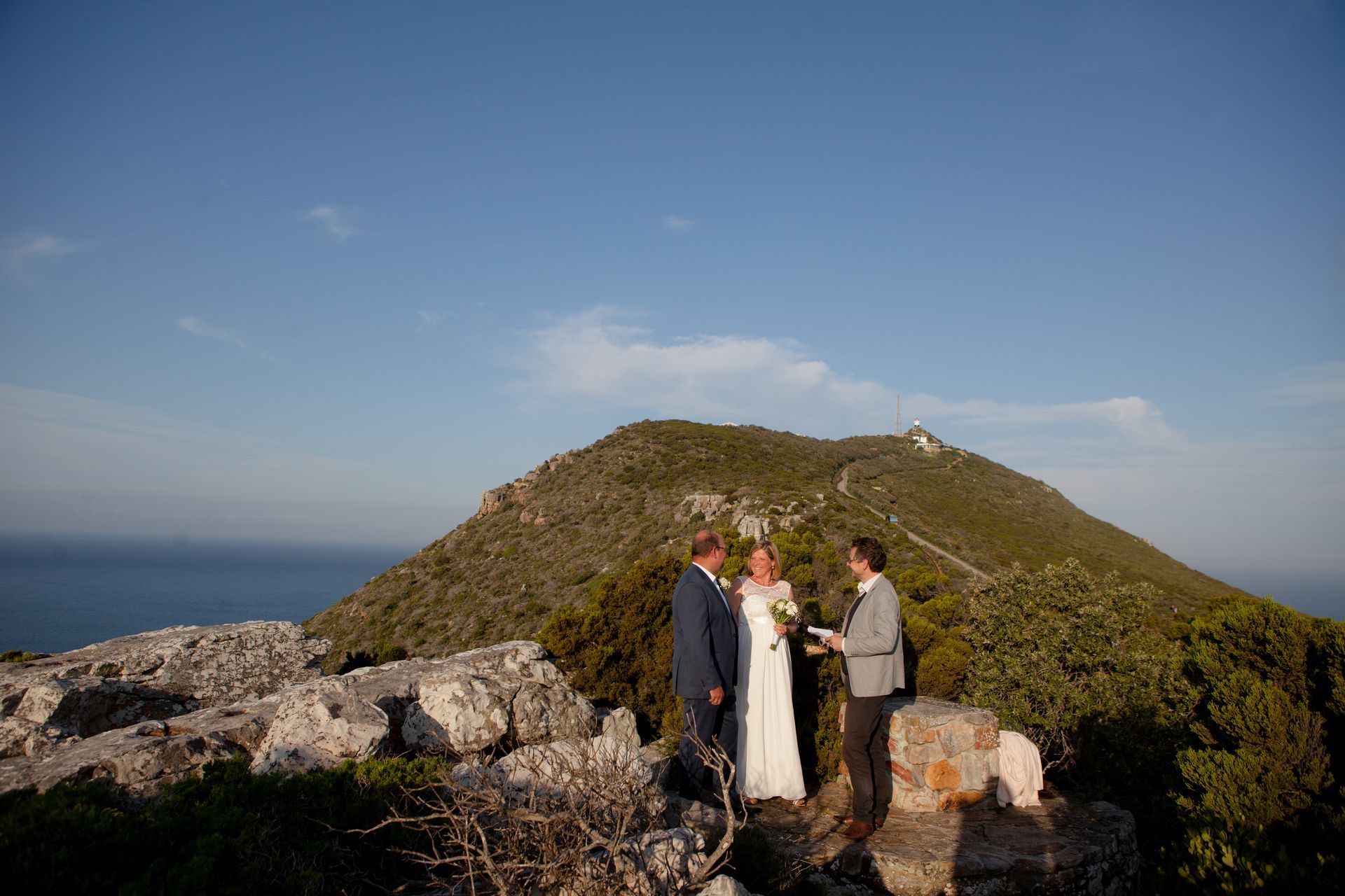 A bride and groom are getting married on top of a mountain overlooking the ocean.