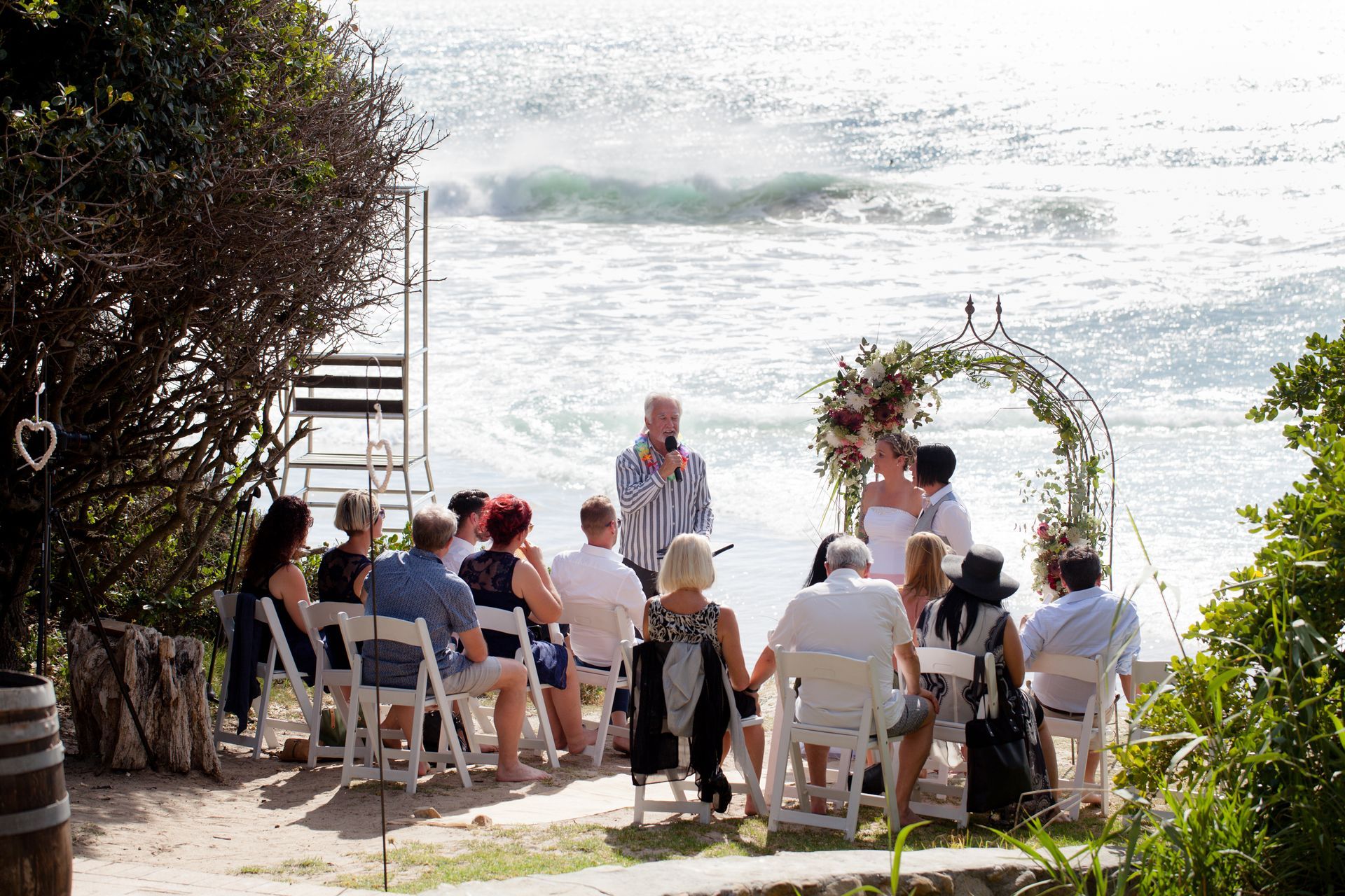 A group of people are sitting in chairs watching a wedding ceremony on the beach.