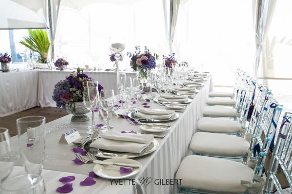 A long table set for a wedding reception with purple flowers on it