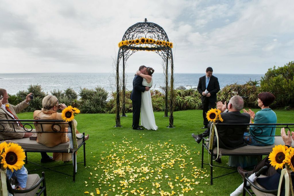 A bride and groom are kissing under a gazebo at their wedding ceremony.