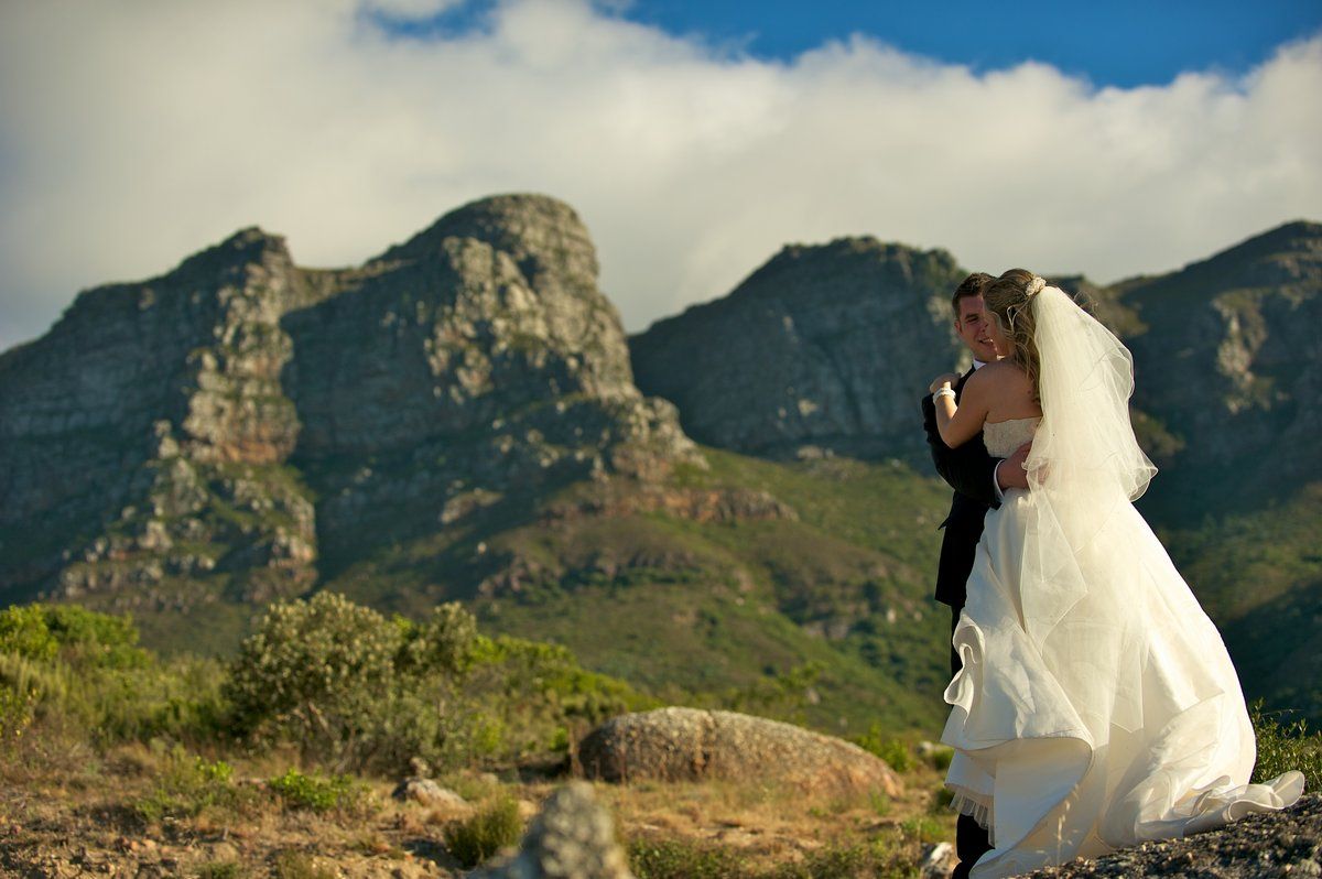 A bride and groom are standing in front of a mountain.