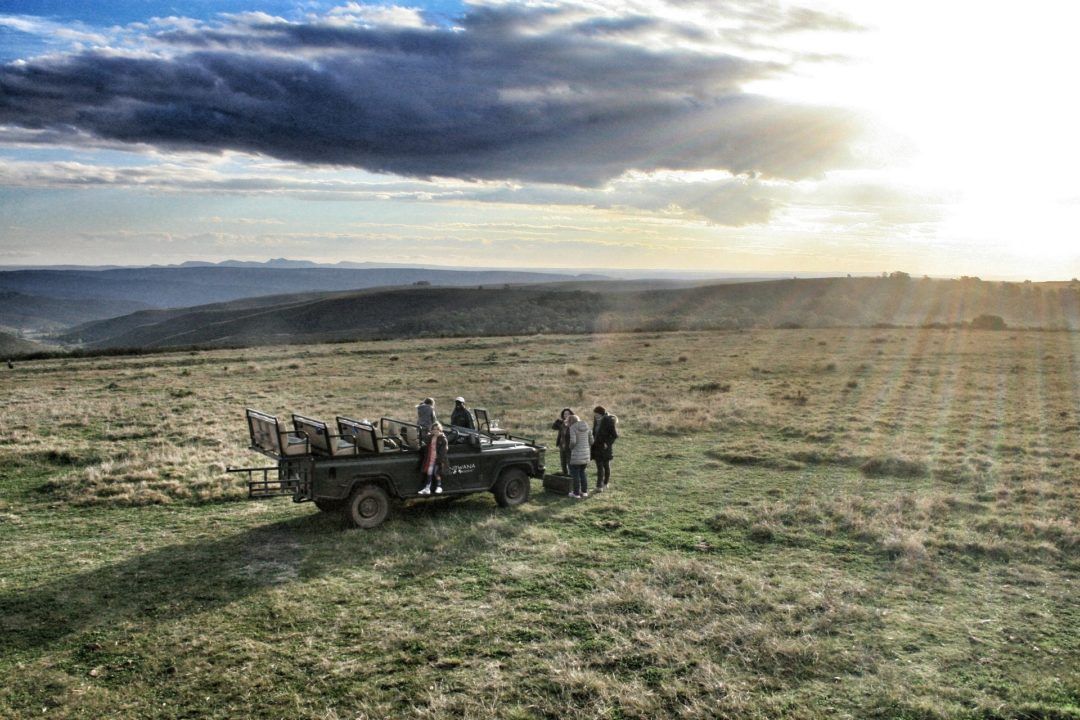 A group of people are standing next to a jeep in a field.