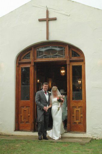 A bride and groom are standing in front of a church with a cross on it