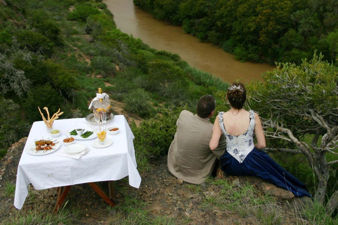 A man and a woman are sitting on a hill overlooking a river.