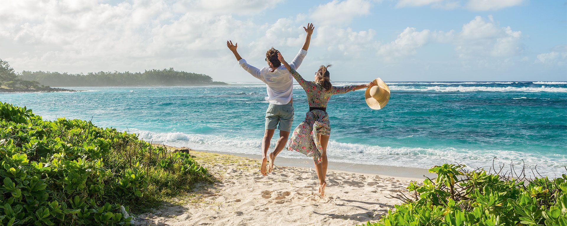 A man and a woman are jumping in the air on a beach.