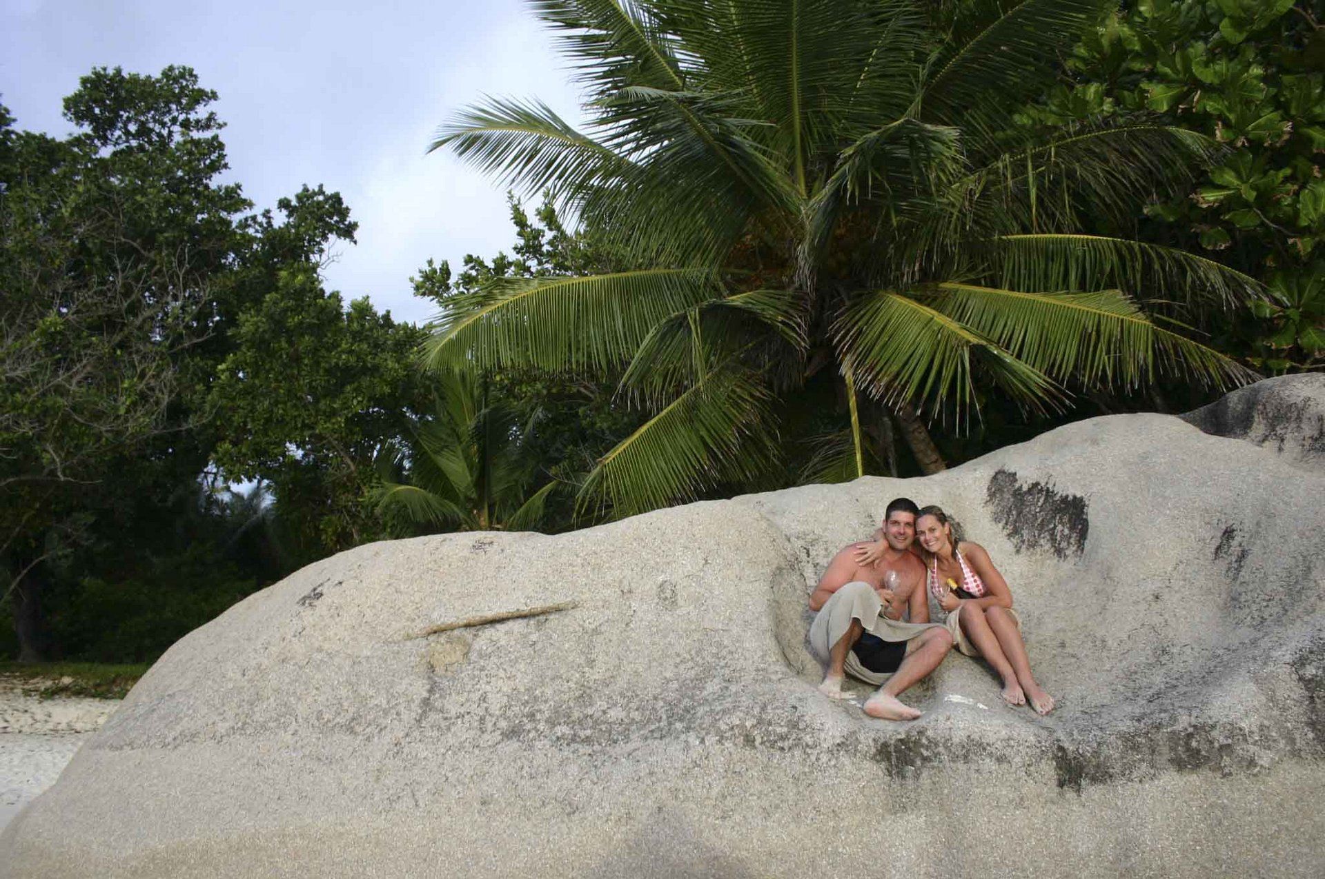 A man and a woman are sitting on top of a large rock