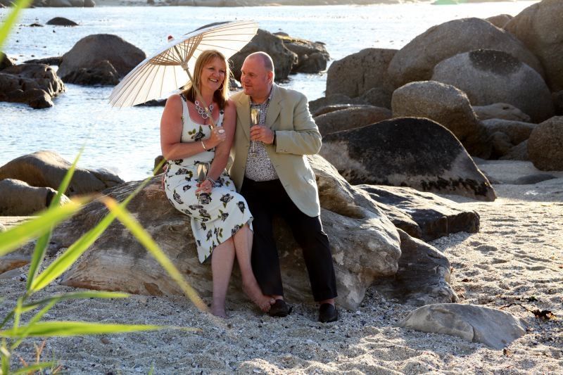 A man and a woman are sitting on a rock on the beach