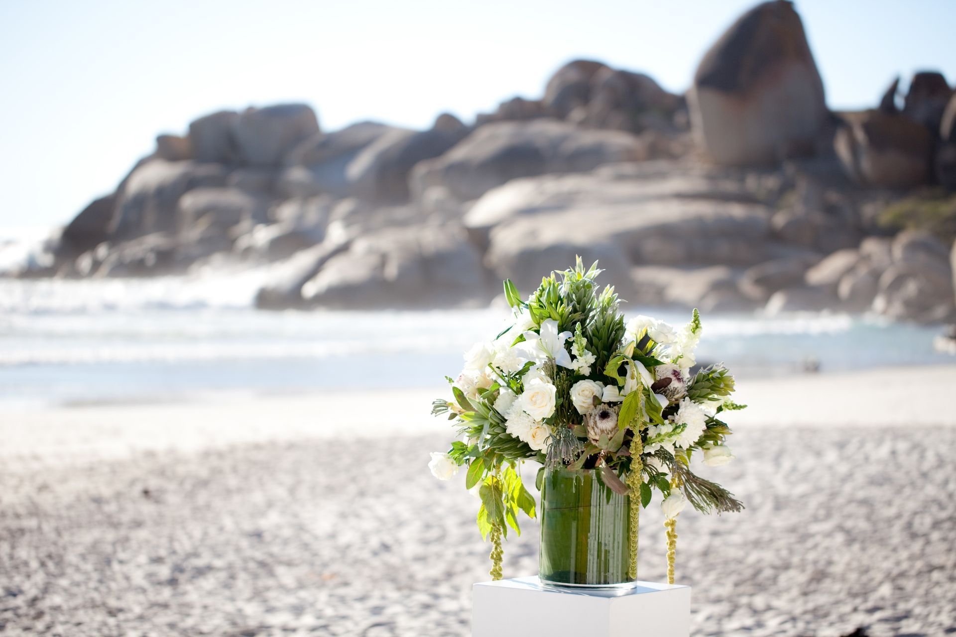 A vase of flowers is sitting on a table on the beach.