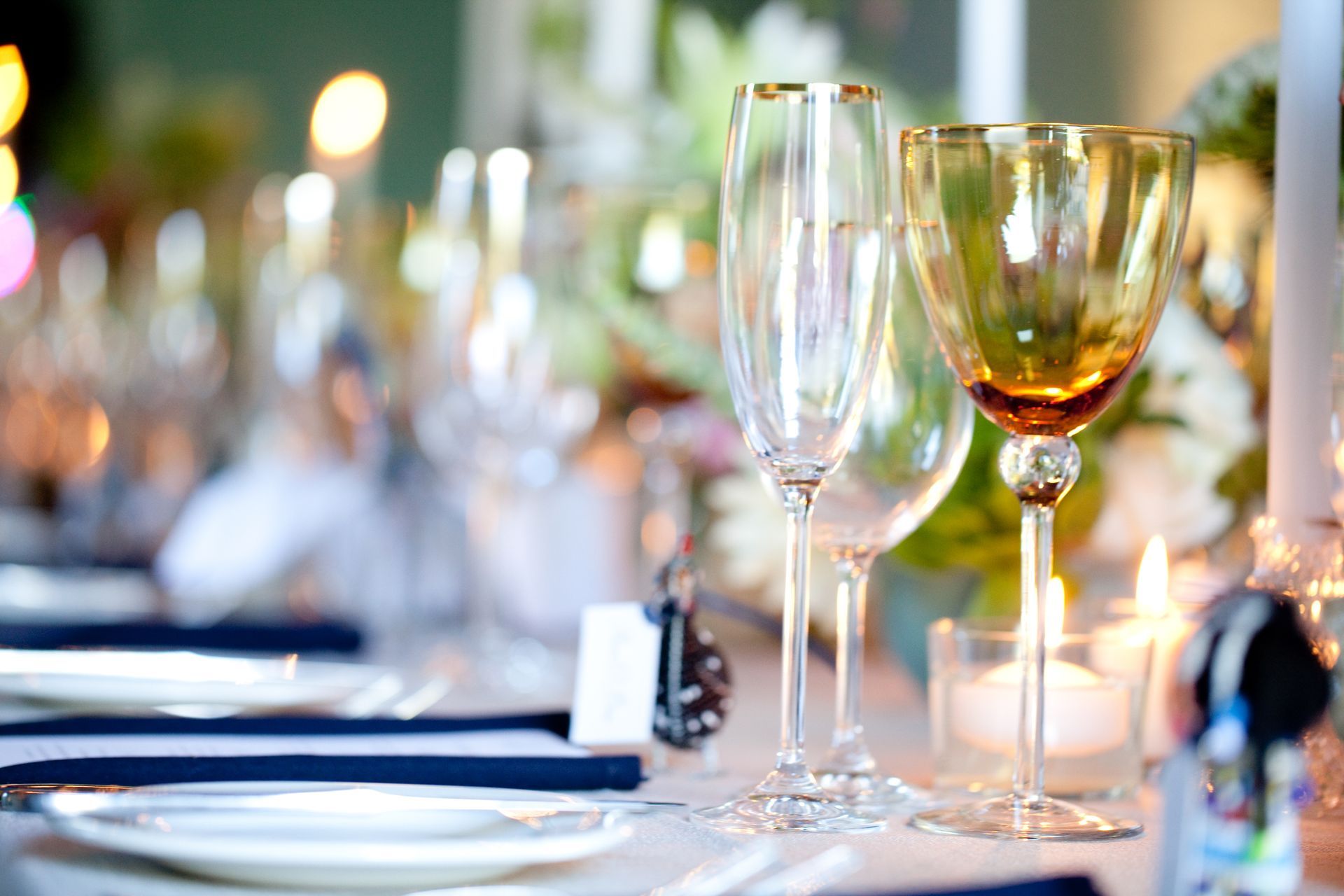 Two wine glasses are sitting on a table with plates and napkins.