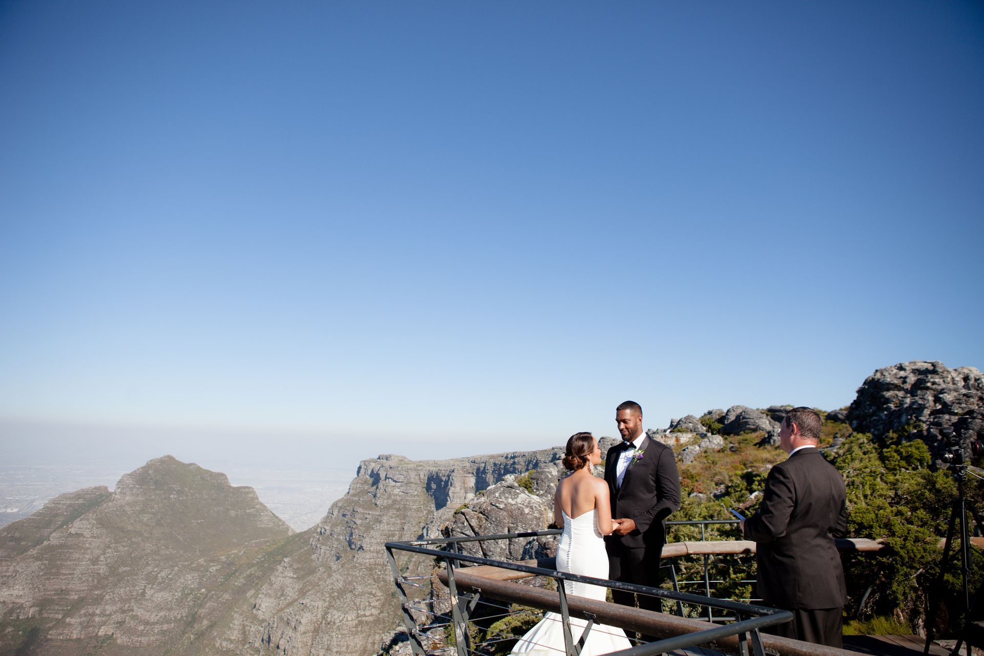 A bride and groom are standing on a balcony overlooking a mountain.