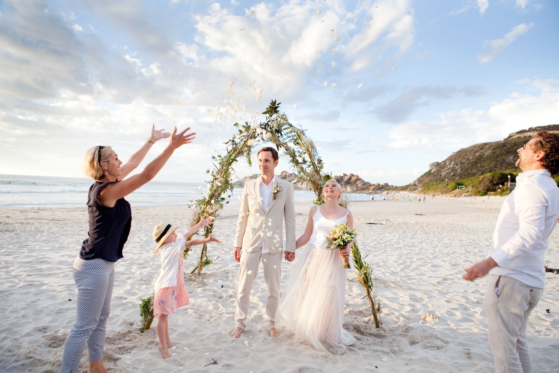 A bride and groom are standing under a wedding arch on the beach.