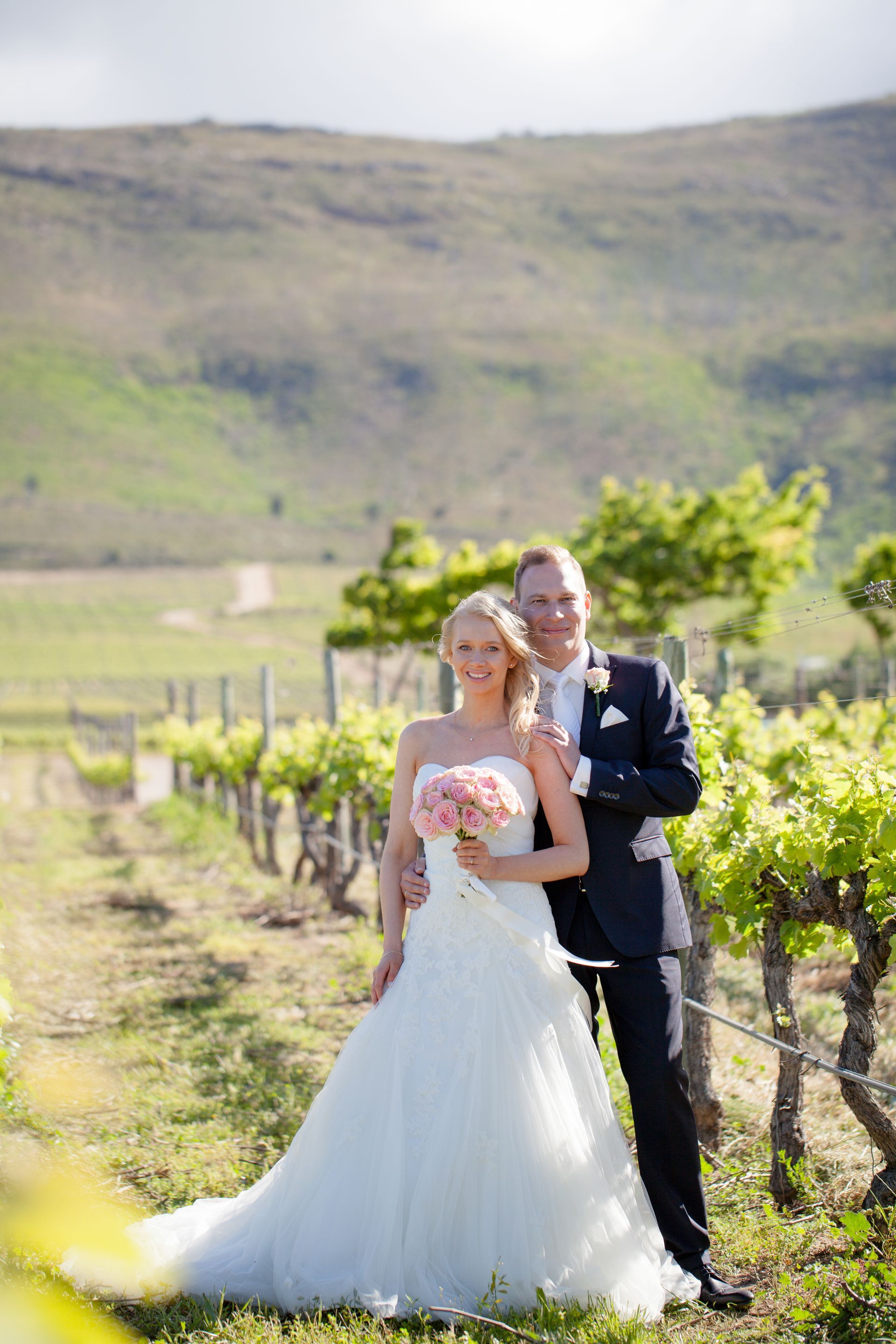 A bride and groom are posing for a picture in a vineyard.