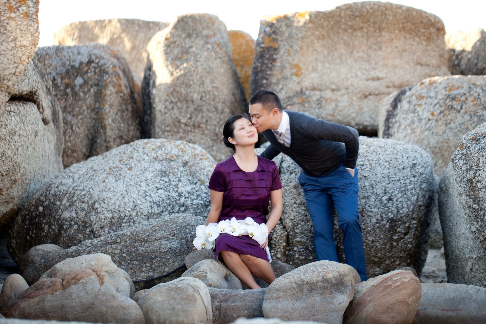 A man is kissing a woman on the forehead while sitting on a pile of rocks.