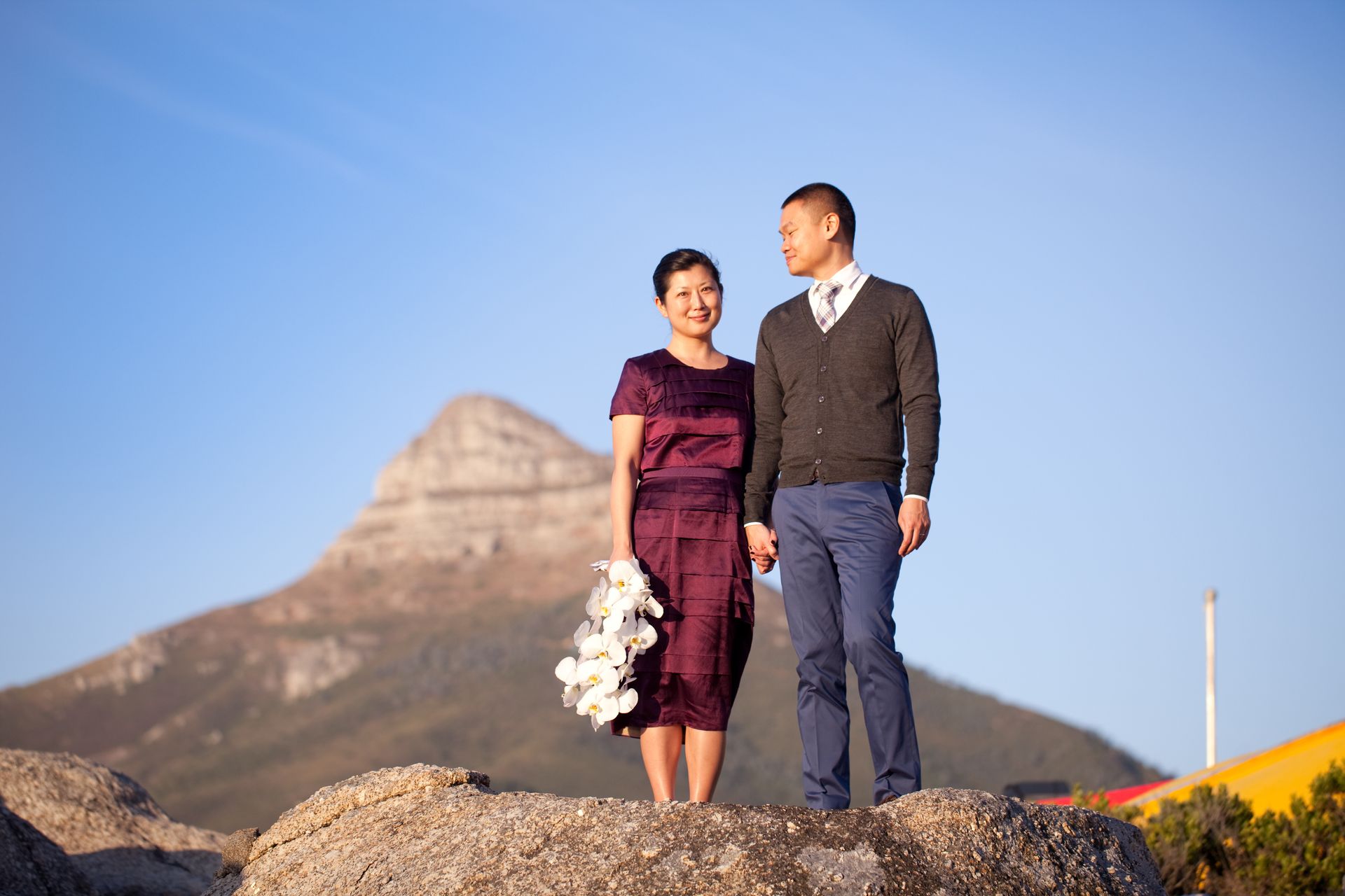 A man and a woman are standing on top of a rock holding hands.