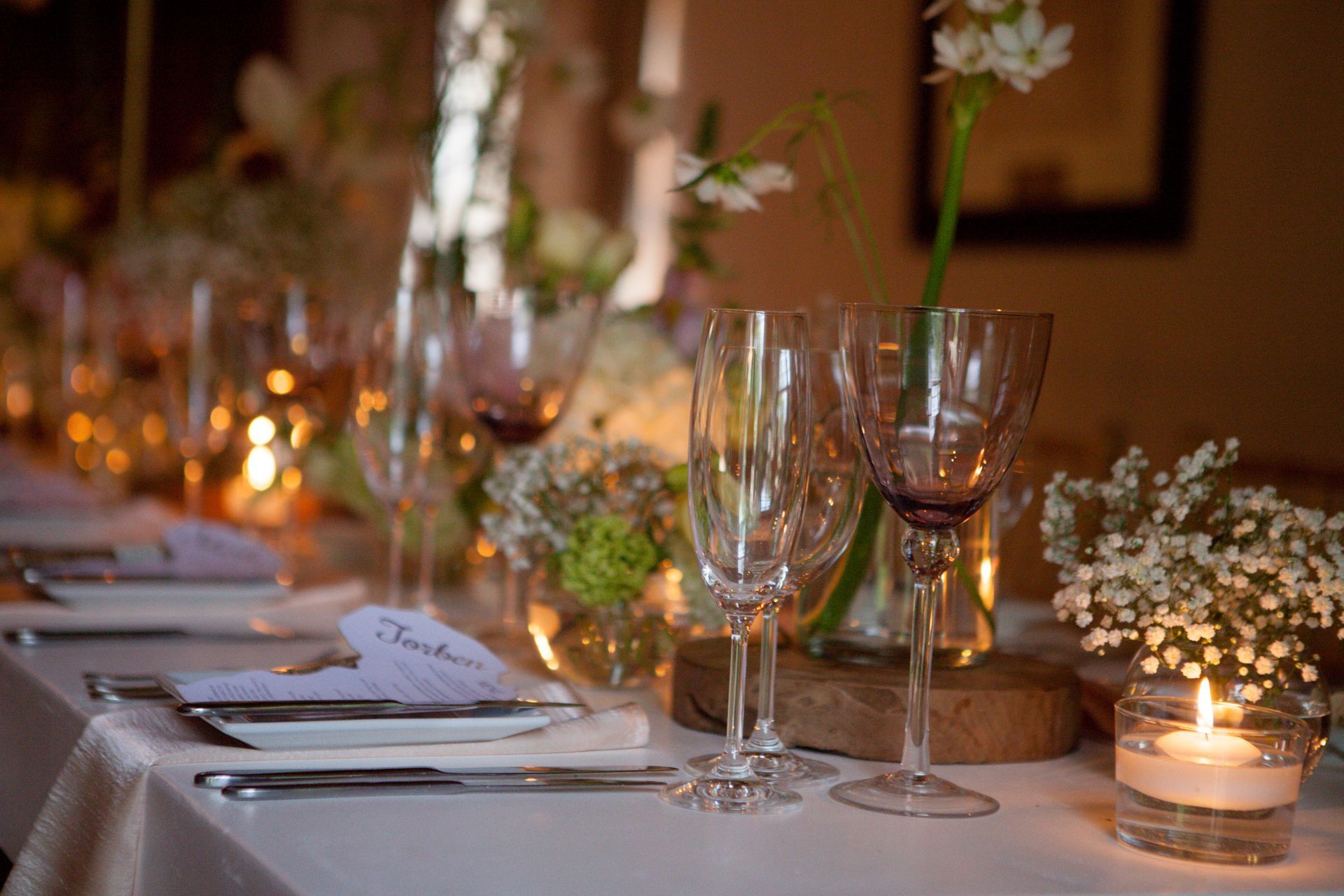 A table set for a wedding reception with wine glasses and candles.