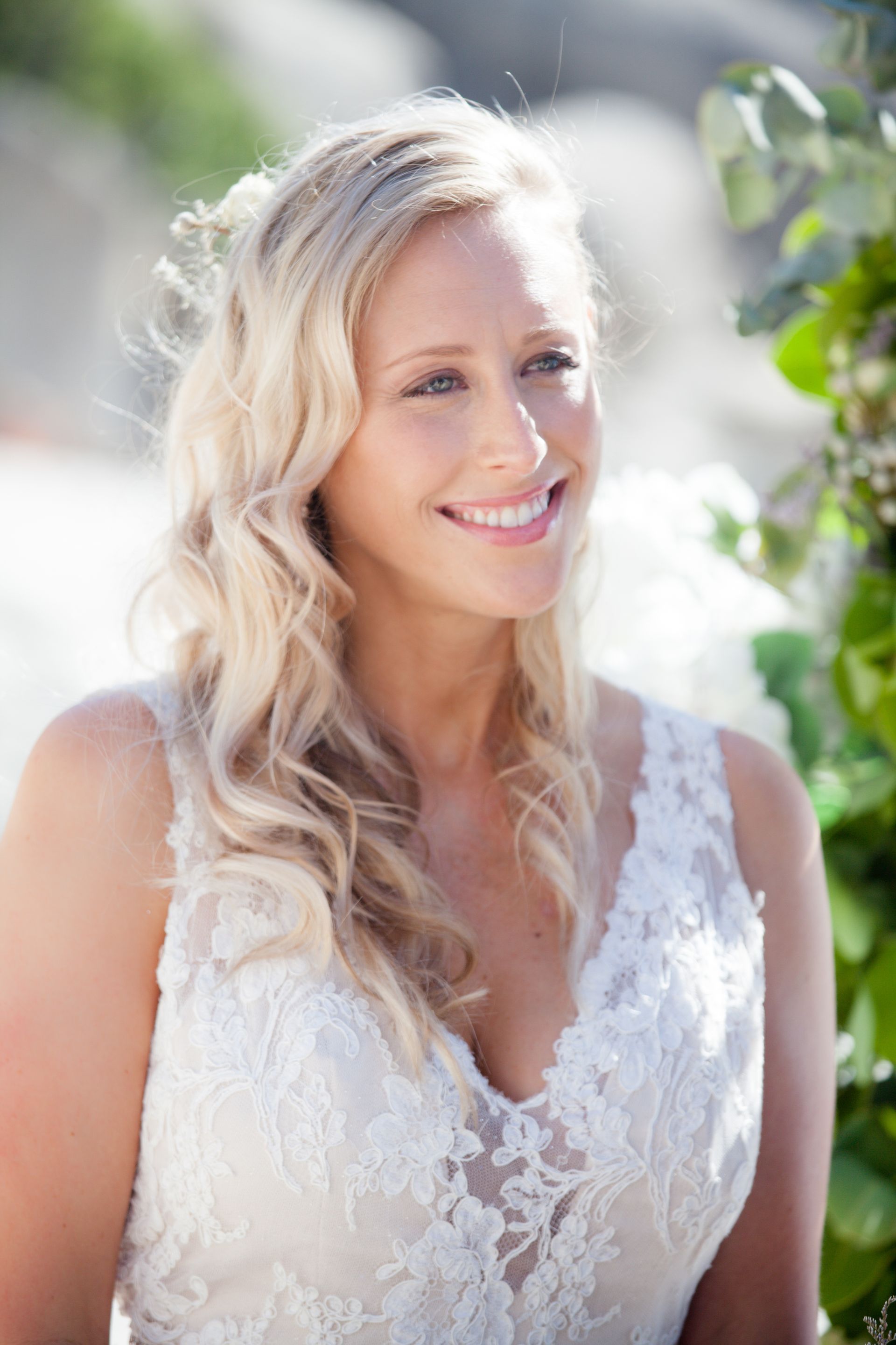 The bride is wearing a white lace wedding dress and smiling.