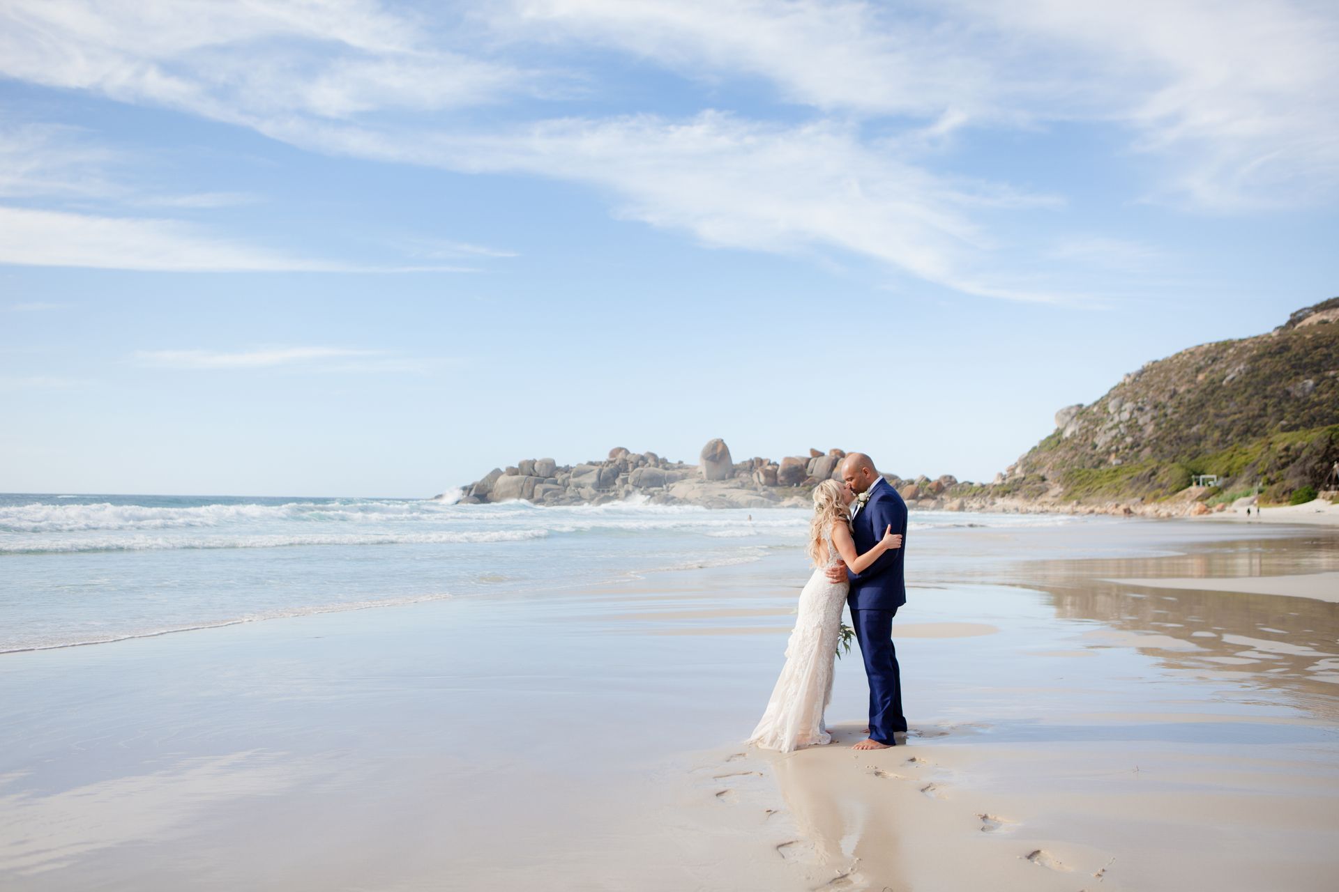 A bride and groom are kissing on the beach.