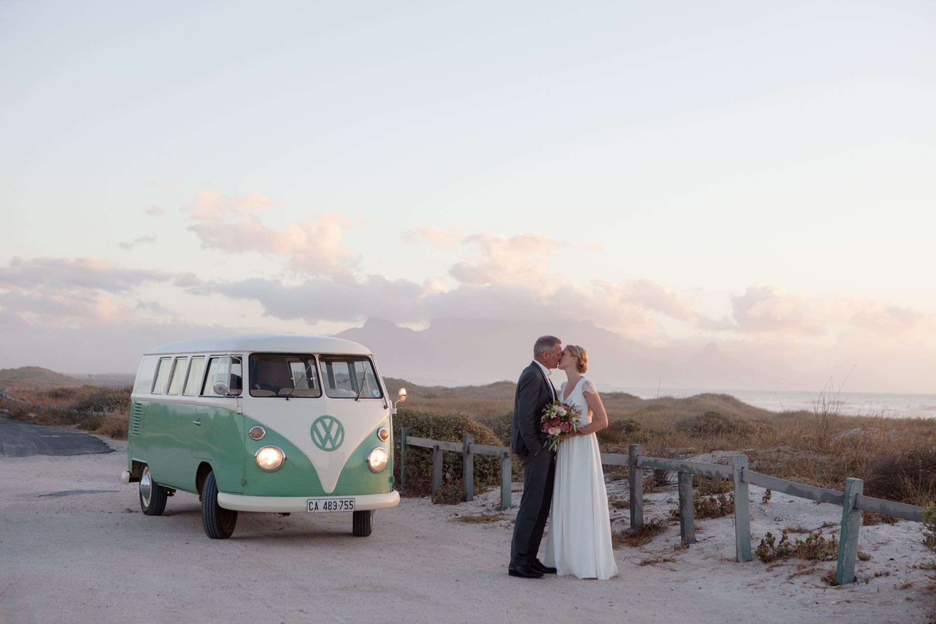 A bride and groom kissing in front of a vw van.