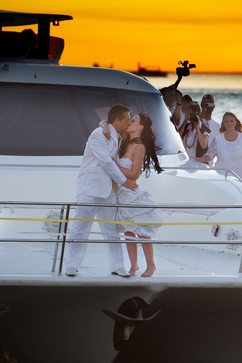 A bride and groom kissing on a boat at sunset