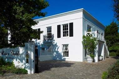 A large white house with black shutters is surrounded by trees.
