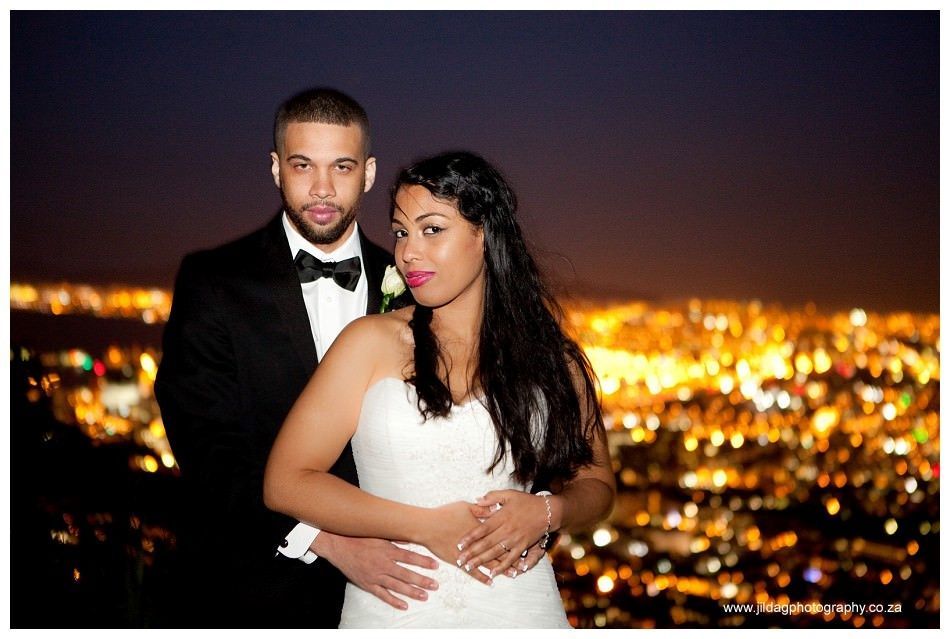 A bride and groom are posing for a picture in front of a city at night.