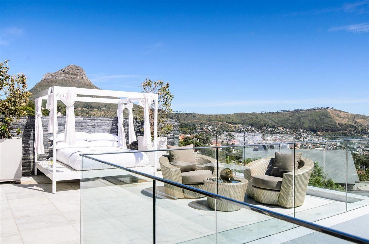 A balcony with a canopy bed and chairs overlooking a city.