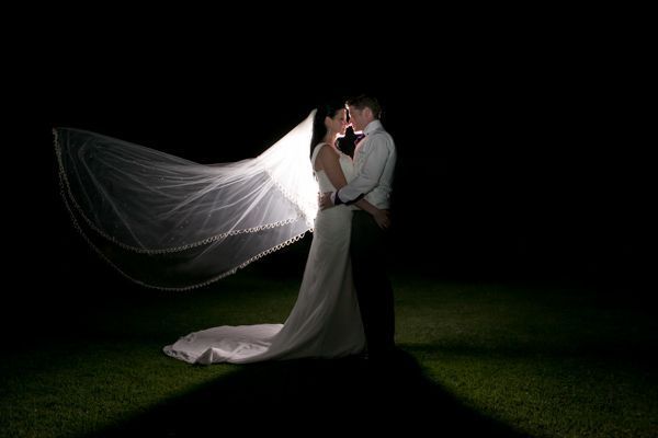A bride and groom are kissing in the dark with their veil blowing in the wind.