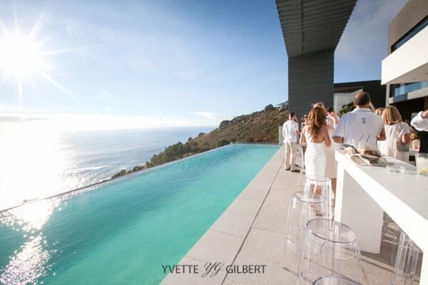 A group of people standing around a swimming pool with a view of the ocean