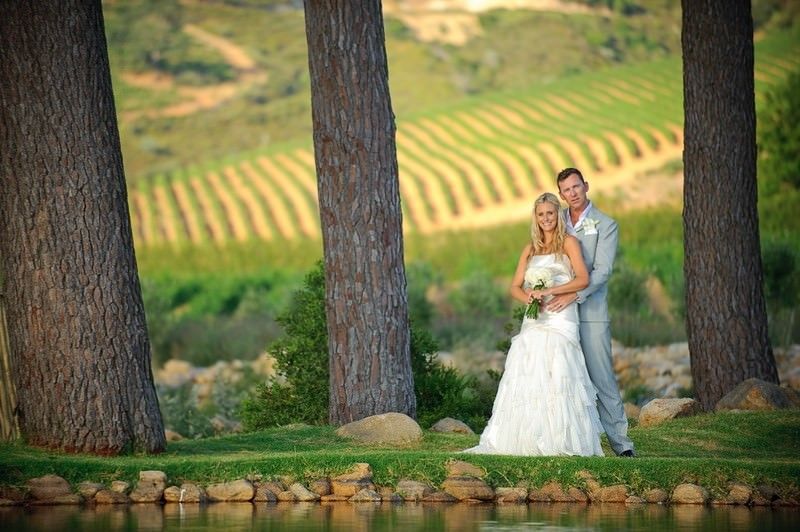 A bride and groom are posing for a picture in front of a lake.