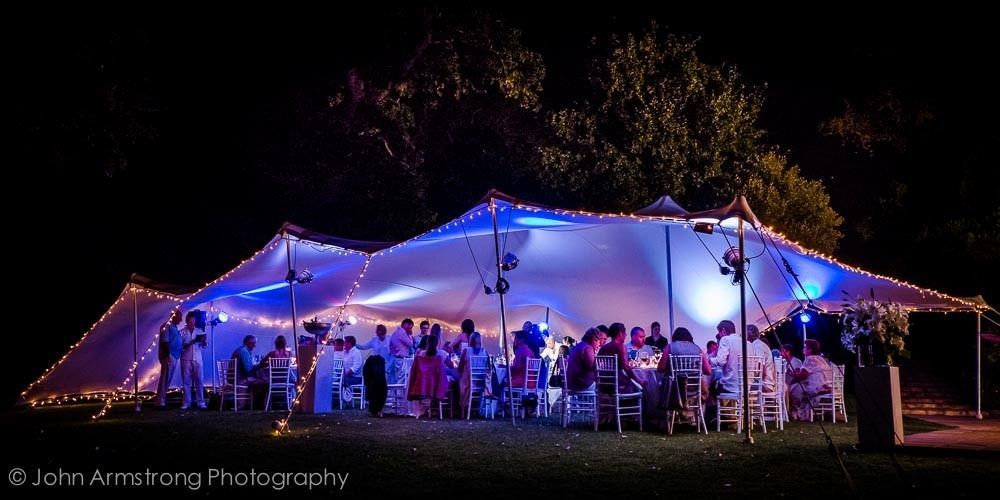 A group of people are sitting under a tent at night.
