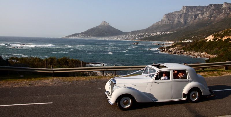 A white car is driving down a road next to the ocean.