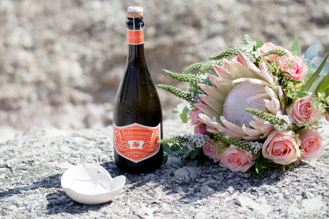 A bottle of wine and a bouquet of flowers are sitting on a rock.