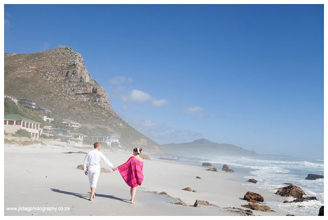 A man and a woman are walking on the beach holding hands.