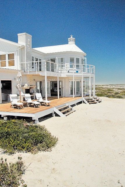 A large white house is sitting on top of a sandy beach.