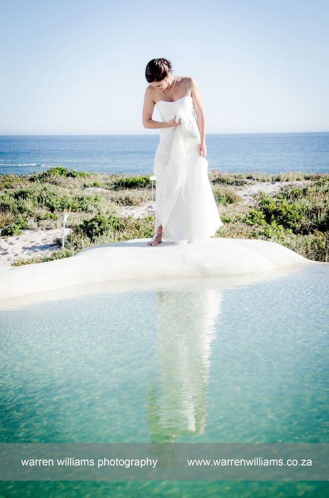 A woman in a white dress is standing on a ledge overlooking the ocean.