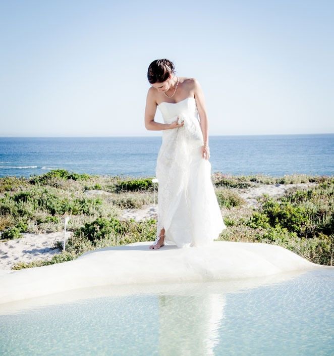 A woman in a white dress is standing in front of a body of water