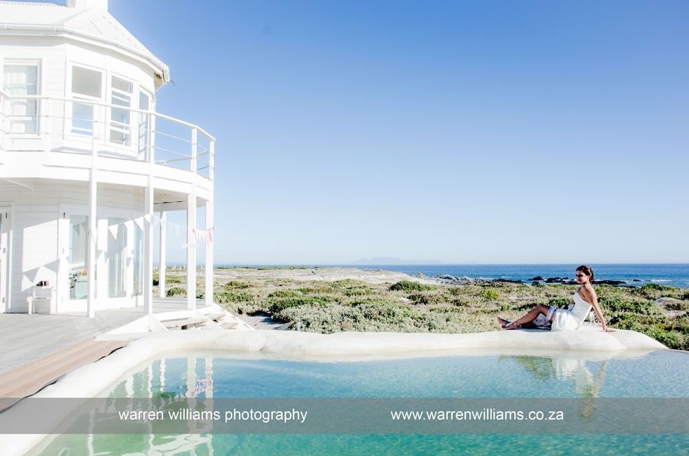 A woman in a wedding dress is sitting on the edge of a swimming pool.