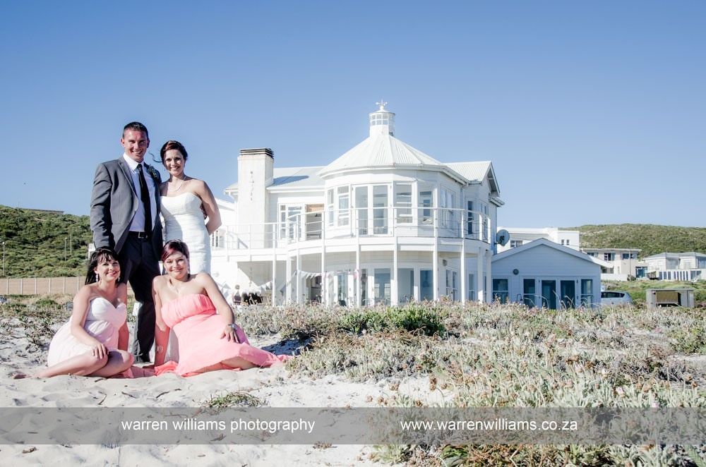 A bride and groom are posing for a picture in front of a large white house.