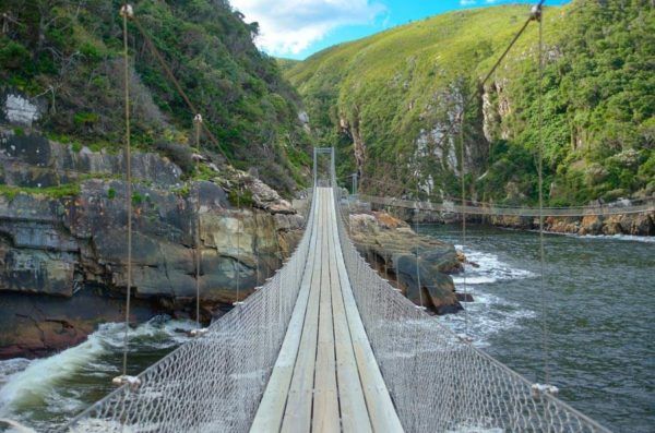 A suspension bridge over a river in the middle of a valley.